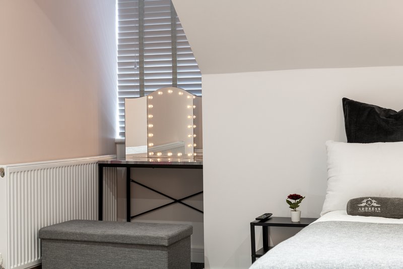 Bedroom with double bed, grey ottoman, mirror with lights, and window with shutters