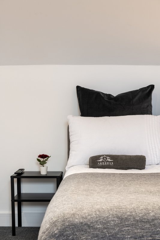 Minimalist bedroom with black pillow, white pillows, beige bedding, and black bedside table