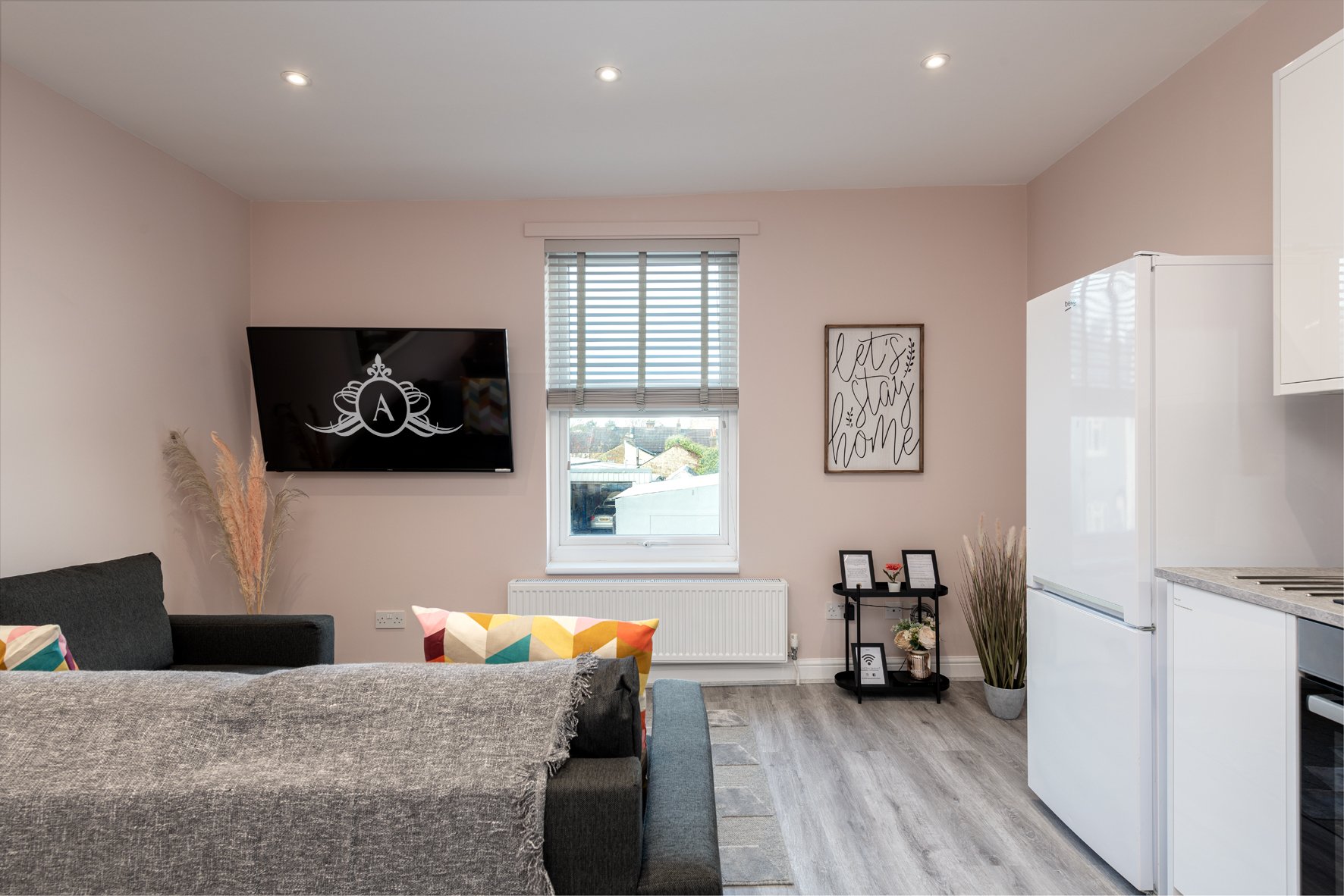 Open-plan living space with grey sofa, kitchen area, wall-mounted TV, and large window