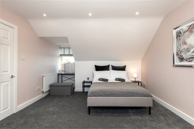 Spacious bedroom with double bed, black headboard, grey carpet and pink walls