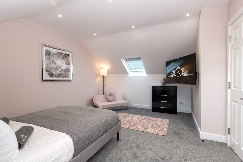 Spacious attic bedroom with double bed, pink armchair, black dresser and skylight window