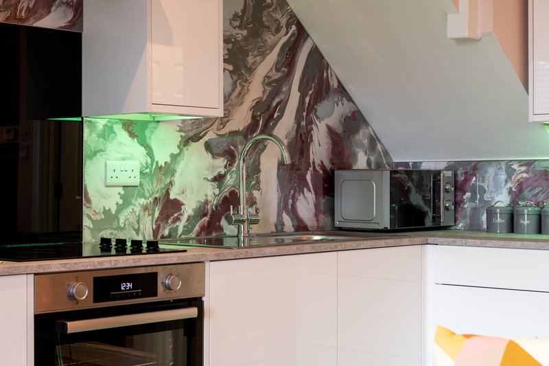 Modern kitchen with white cabinetry, built-in oven, marble backsplash and green accent lighting