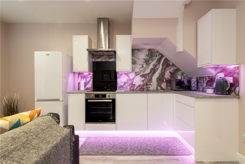 Modern kitchen with white cabinetry, black appliances, and purple ambient lighting