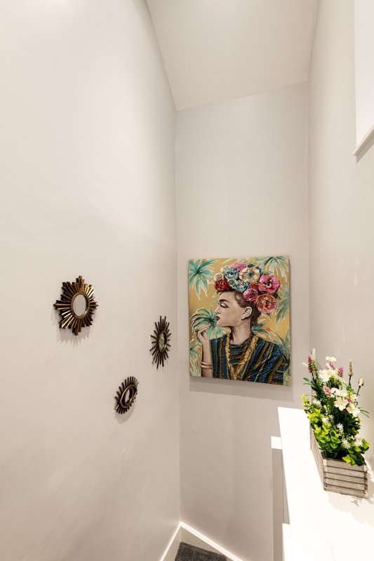 White hallway with decorative wall art, floral portrait, woven wall hangings, and potted flowers