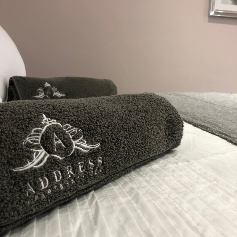 Bedroom with dark towels featuring embroidered branding on white bedding