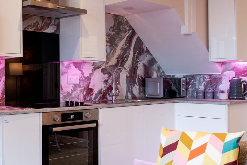 Modern kitchen with white cabinetry, black oven, pink backlighting, and geometric patterned cushion
