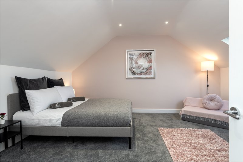 Bright attic bedroom with double bed, grey carpet, pink accents and framed wall art