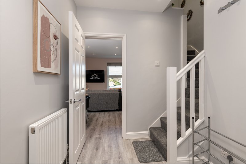 Hallway with white doors, radiator, wooden flooring and staircase leading upstairs