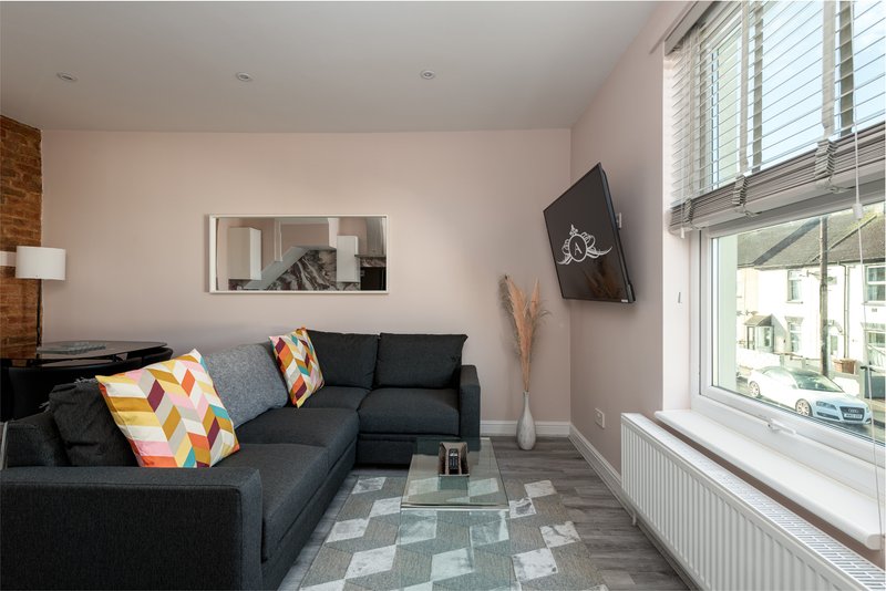 Modern living room with dark corner sofa, colorful cushions, wall-mounted TV, and large windows