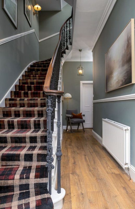 Staircase with tartan runner and wooden handrail, hallway with grey walls and pendant lights