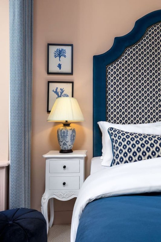 Bedroom with blue upholstered headboard, white nightstand, table lamp, and framed botanical wall art