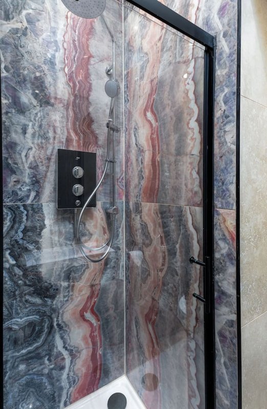 Modern bathroom shower enclosure with marble-effect tiled walls and black fixtures