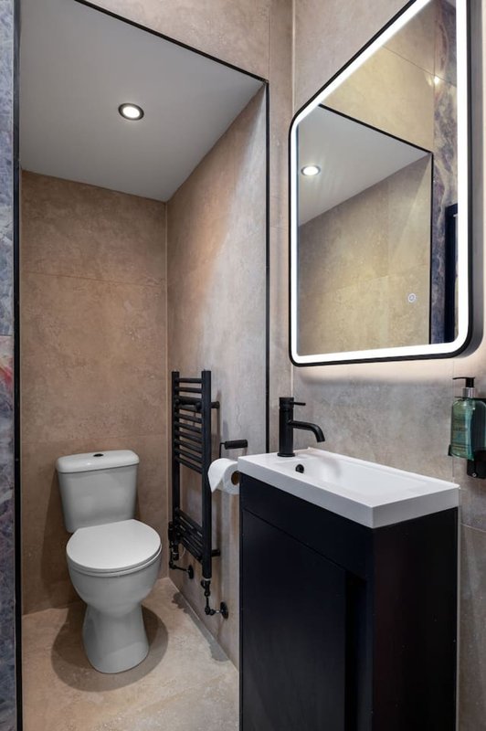 Modern bathroom with toilet, black vanity, white sink and illuminated mirror
