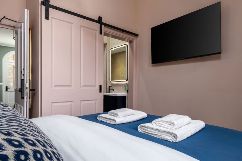 Modern bedroom with blue bed, white towels, wall-mounted TV and pink sliding barn doors