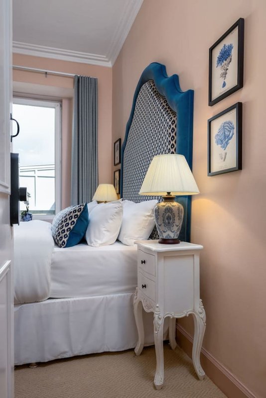 Bedroom with blue upholstered headboard, white bedding, side table lamp, and framed botanical prints