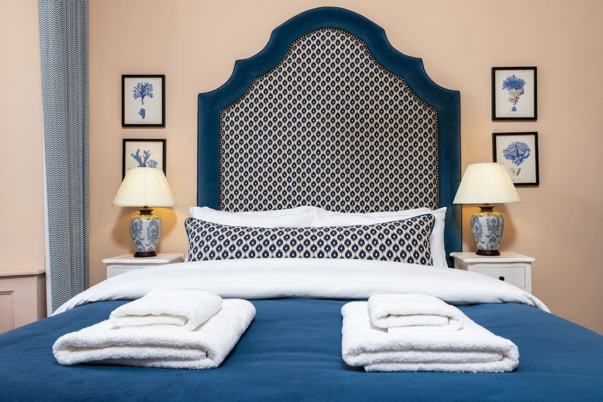 Bedroom with blue upholstered headboard, white pillows, blue bedding, and decorative wall art