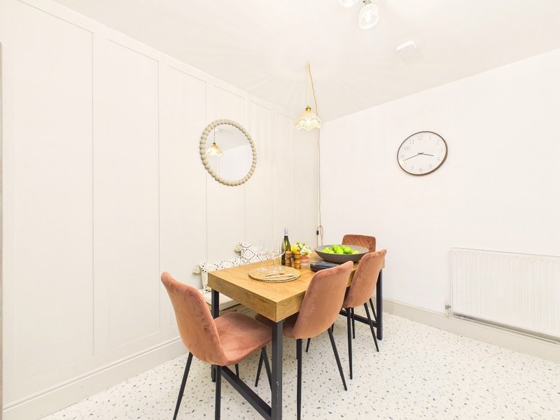 Bright dining room with wooden table, tan upholstered chairs, pendant light and wall clocks