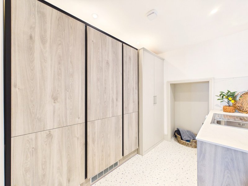 Modern laundry room with built-in wooden cabinetry, white counter, and appliances