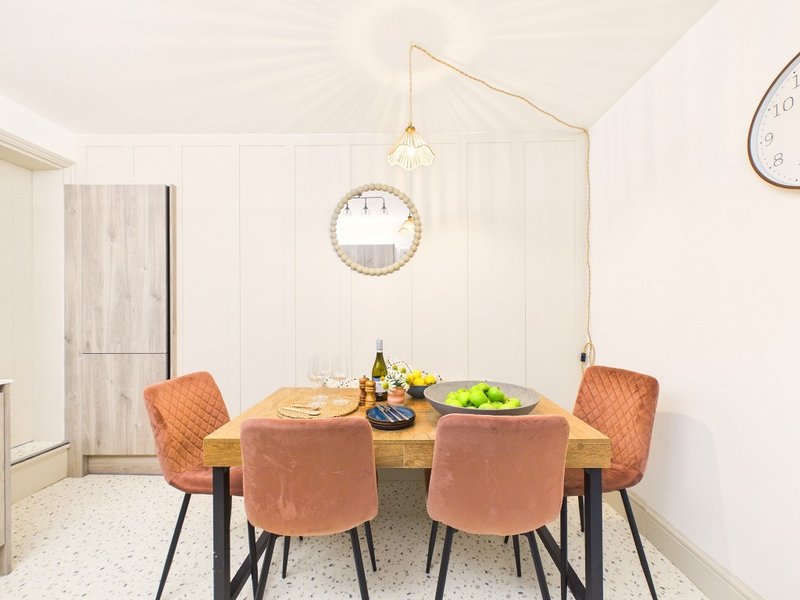 Dining room with round wooden table, four upholstered chairs, pendant light and wall clock