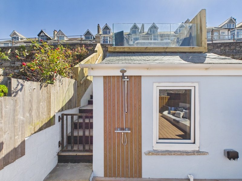 White exterior building with wooden door, window, and rooftop access, seafront residential backdrop