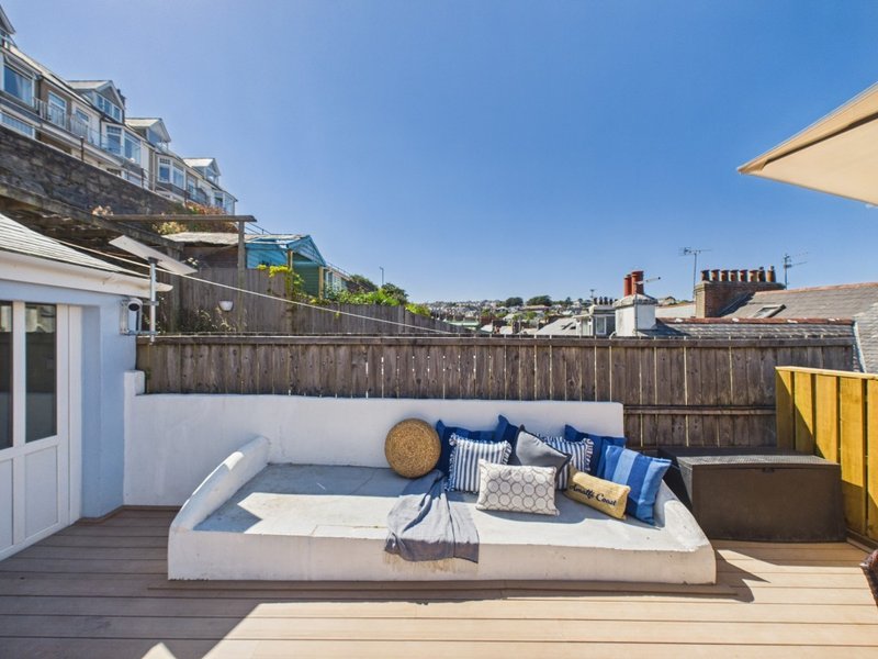 Rooftop terrace with daybed, cushions, and yellow parasol overlooking suburban neighborhood