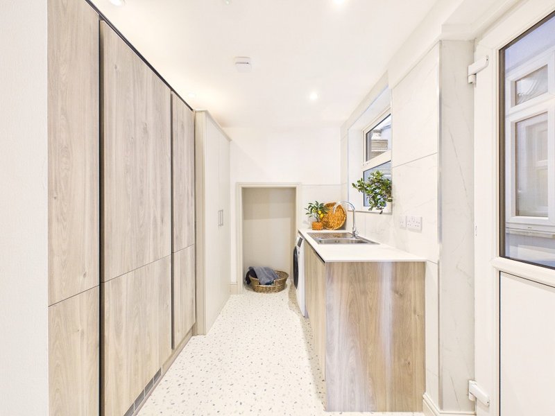 Modern kitchen hallway with wooden cabinetry, white countertop, potted plant and window