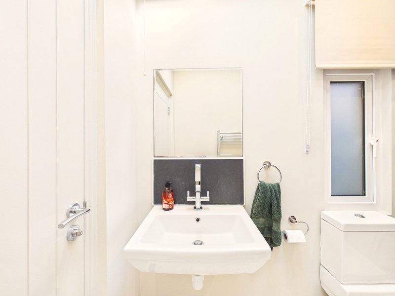 Modern bathroom with white wall-mounted sink, mirror, and green towel hanging on rack