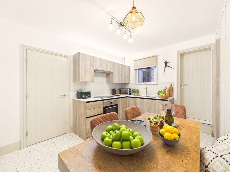 Modern kitchen-diner with wooden cabinets, dining table with fresh fruit, and pendant lighting