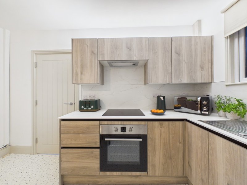 Modern kitchen with wooden cabinetry, built-in oven, stovetop, stainless steel counters and appliances