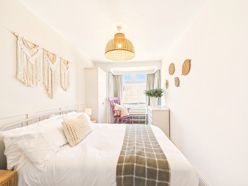 Bright modern bedroom with white bed, woven pendant light, and open balcony door with city view