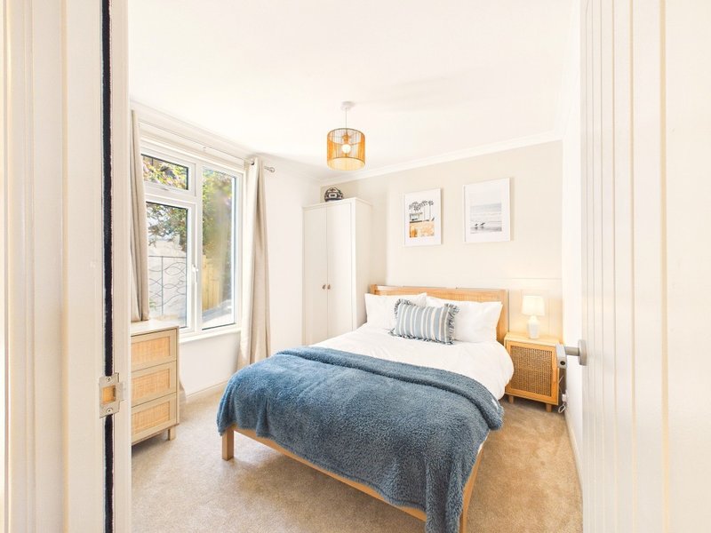 Bright bedroom with double bed, wooden furniture, blue throw and French doors to garden