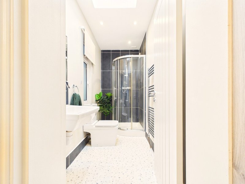 Modern bathroom with corner shower enclosure, white sink, mirror and heated towel rail