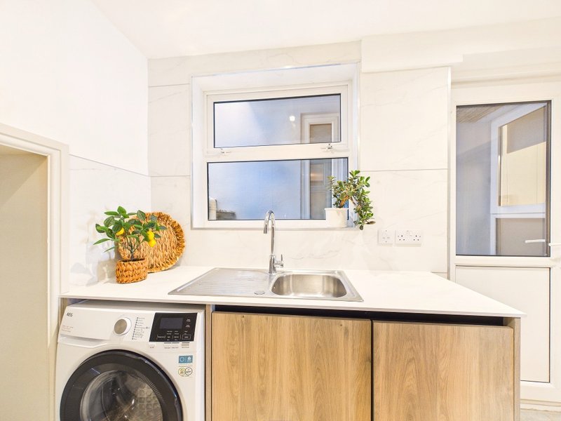 Modern kitchen with sink, washing machine, wooden cabinets and window