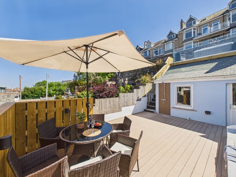 Spacious rooftop terrace with cream umbrella, wicker seating, and coastal townhouse views