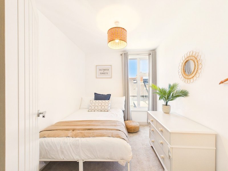 Bright bedroom with single bed, white dresser, rattan pendant light and balcony access