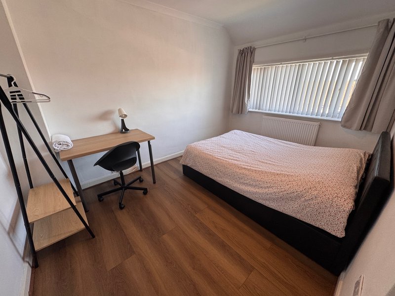 Bedroom with double bed, wooden desk, chair, and vertical blinds window