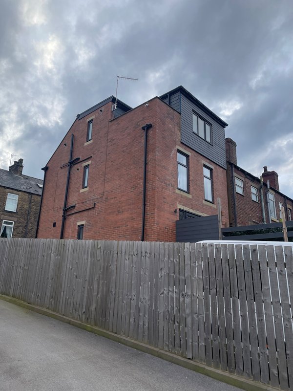 Brick terraced house exterior with white fence and driveway, cloudy sky