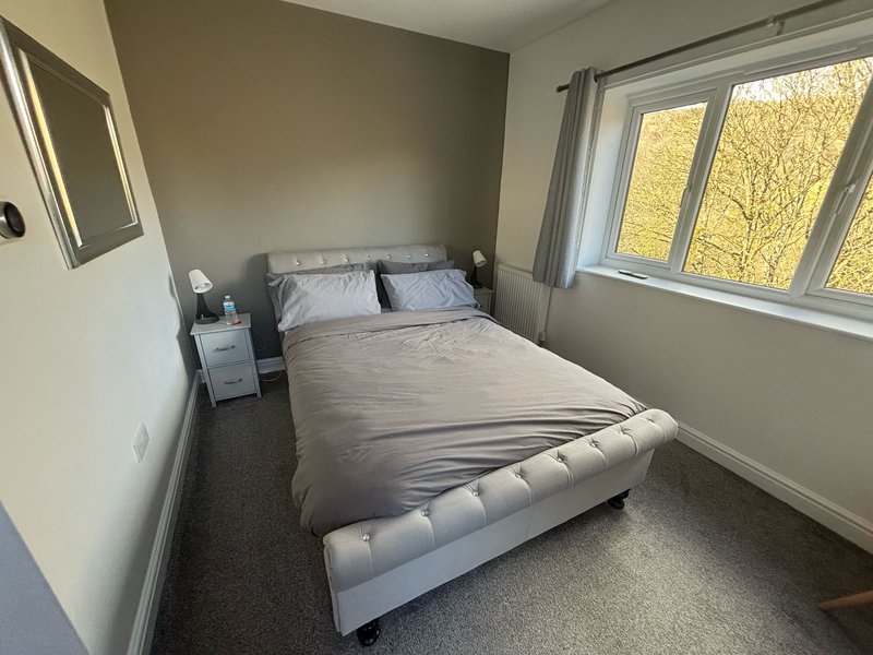 Bedroom with double bed, bedside table, mirror, and large window with autumn tree view