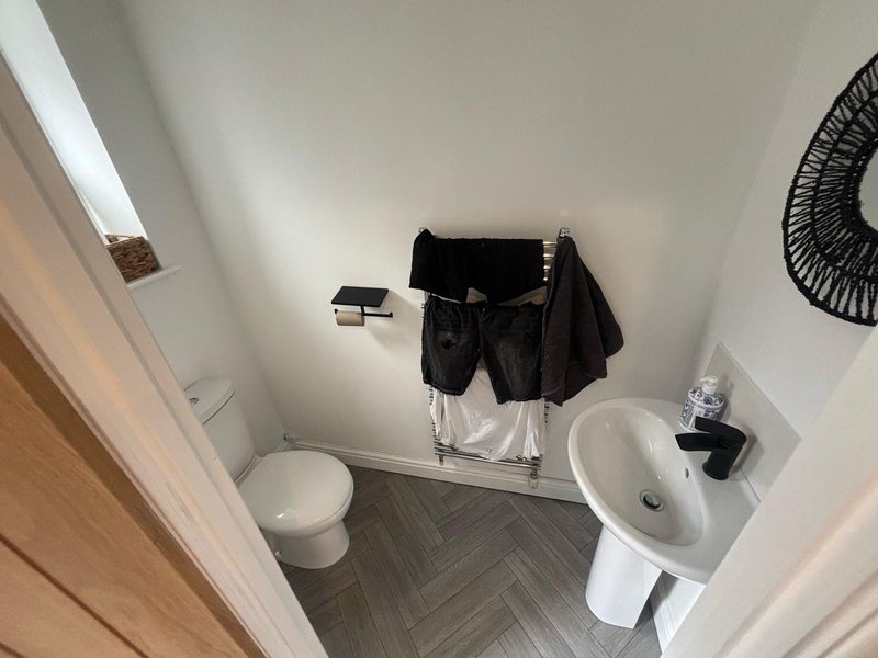 Compact bathroom with toilet, round sink, towel rack with black towels, and small fan