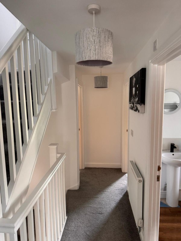Bright hallway with white staircase railing, pendant light fixture, and carpet flooring