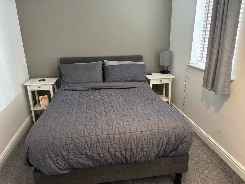 Bedroom with dark gray bed, two white bedside tables, window with gray curtains