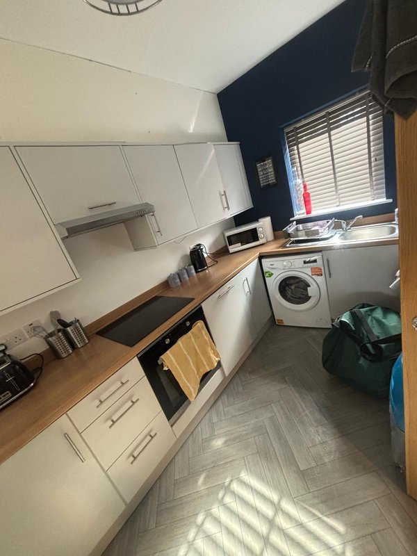 Kitchen with white cabinets, wooden countertop, washing machine, and blue accent wall