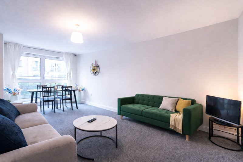 Open-plan living room with beige sofa, green couch, round coffee table, and dining area by windows
