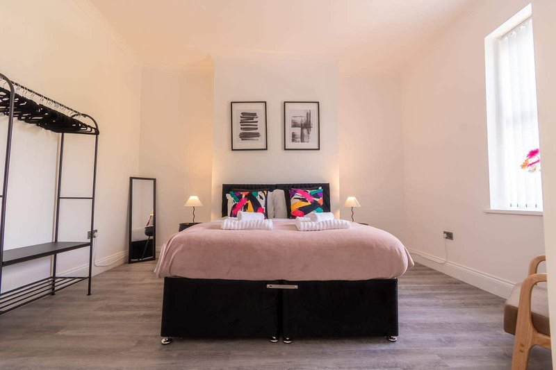 Spacious bedroom with double bed, pink bedding, framed wall art, and natural light from window