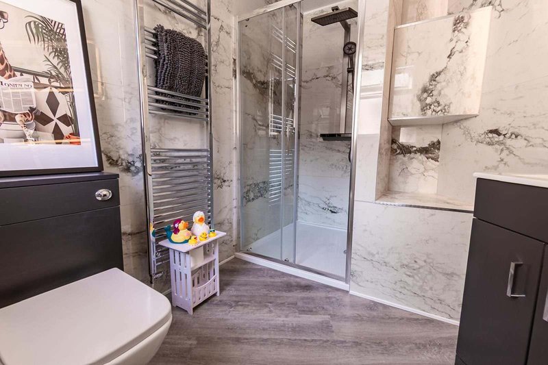 Modern bathroom with walk-in shower, toilet, heated towel rail, and marble-effect tiles