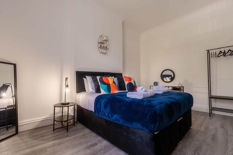 Modern bedroom with blue velvet bed, colorful pillows, wooden flooring and minimalist decor