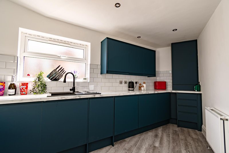 Modern kitchen with dark teal cabinetry, white subway tile splashback, sink and window