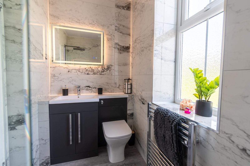 Modern bathroom with black vanity, lit mirror, toilet, heated towel rail and window