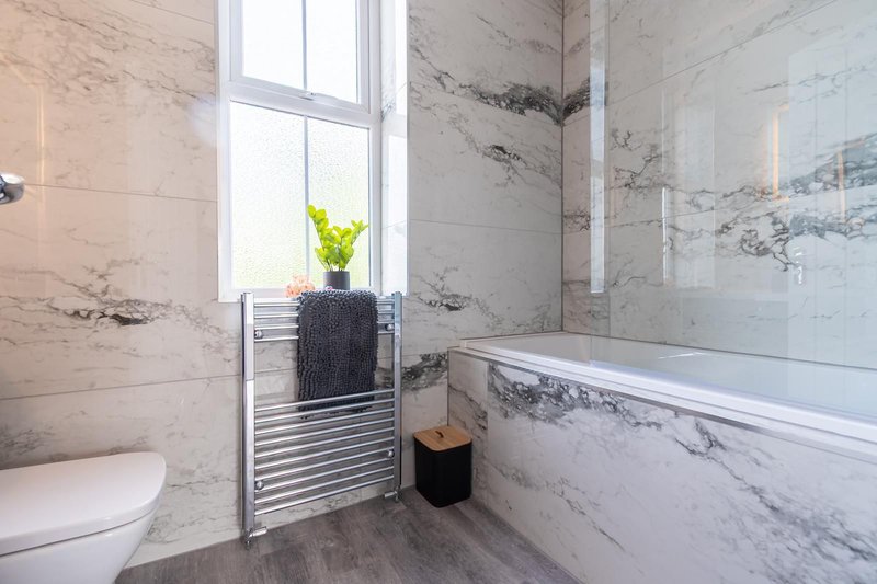 Modern bathroom with marble tiles, heated towel rail, and small potted plant on windowsill
