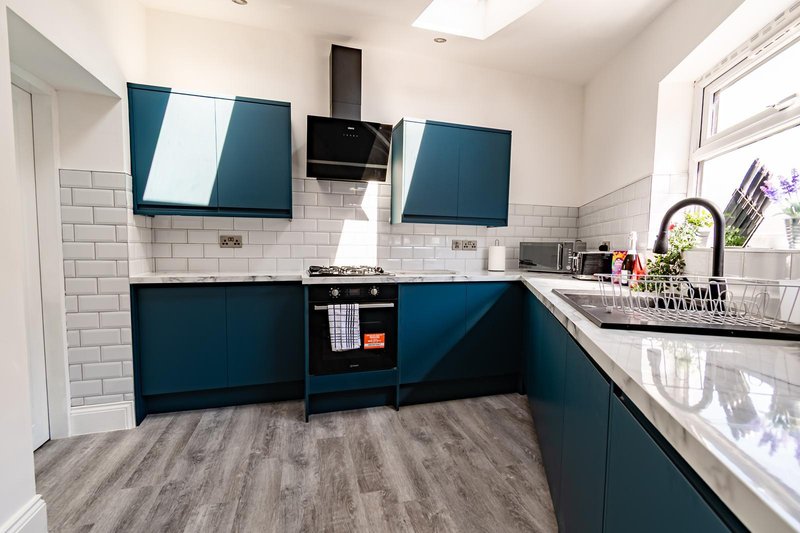 Modern kitchen with teal cabinets, white subway tile splashback, black range hood and grey wood-effect flooring